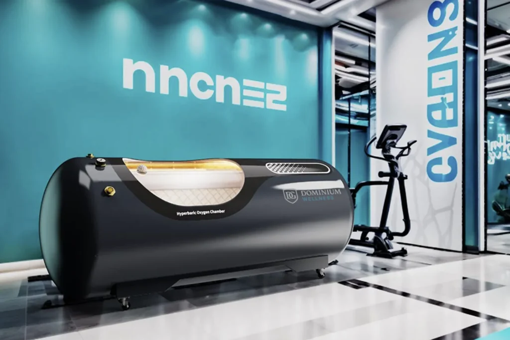 Elegantna hiperbarična kiseonička komora Dominium Wellness, model DW230TCLP, izložena u savremenom wellness centru sa tirkiznim zidovima, sobom ispunjenom svetlošću, biciklom za vežbanje i futurističkim dizajnom.