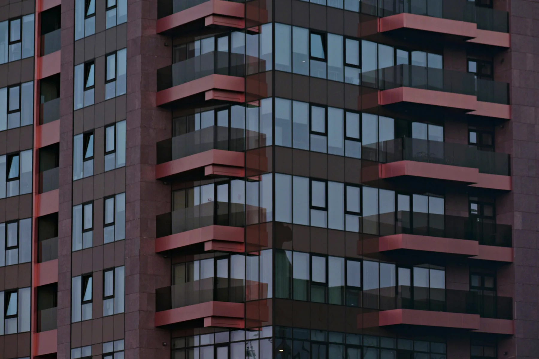 Moderna fasada zgrade sa tamnim staklenim prozorima i balkonima sa ružičastim akcentima, u geometrijskom i urbanom stilu.