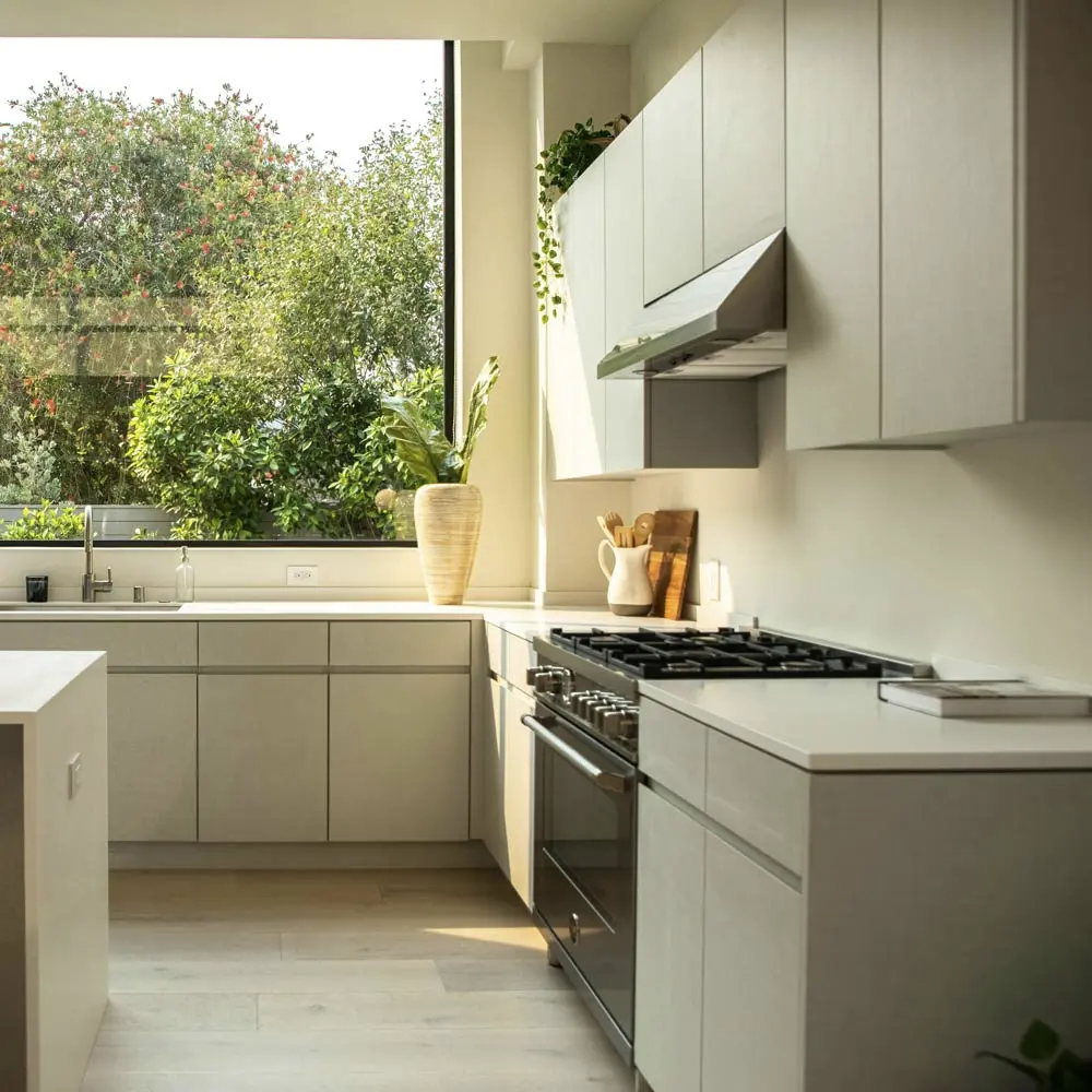 Moderna kuhinja sa svetlosivim elementima, velikim prozorom sa pogledom na zelenilo i obiljem prirodne svetlosti.