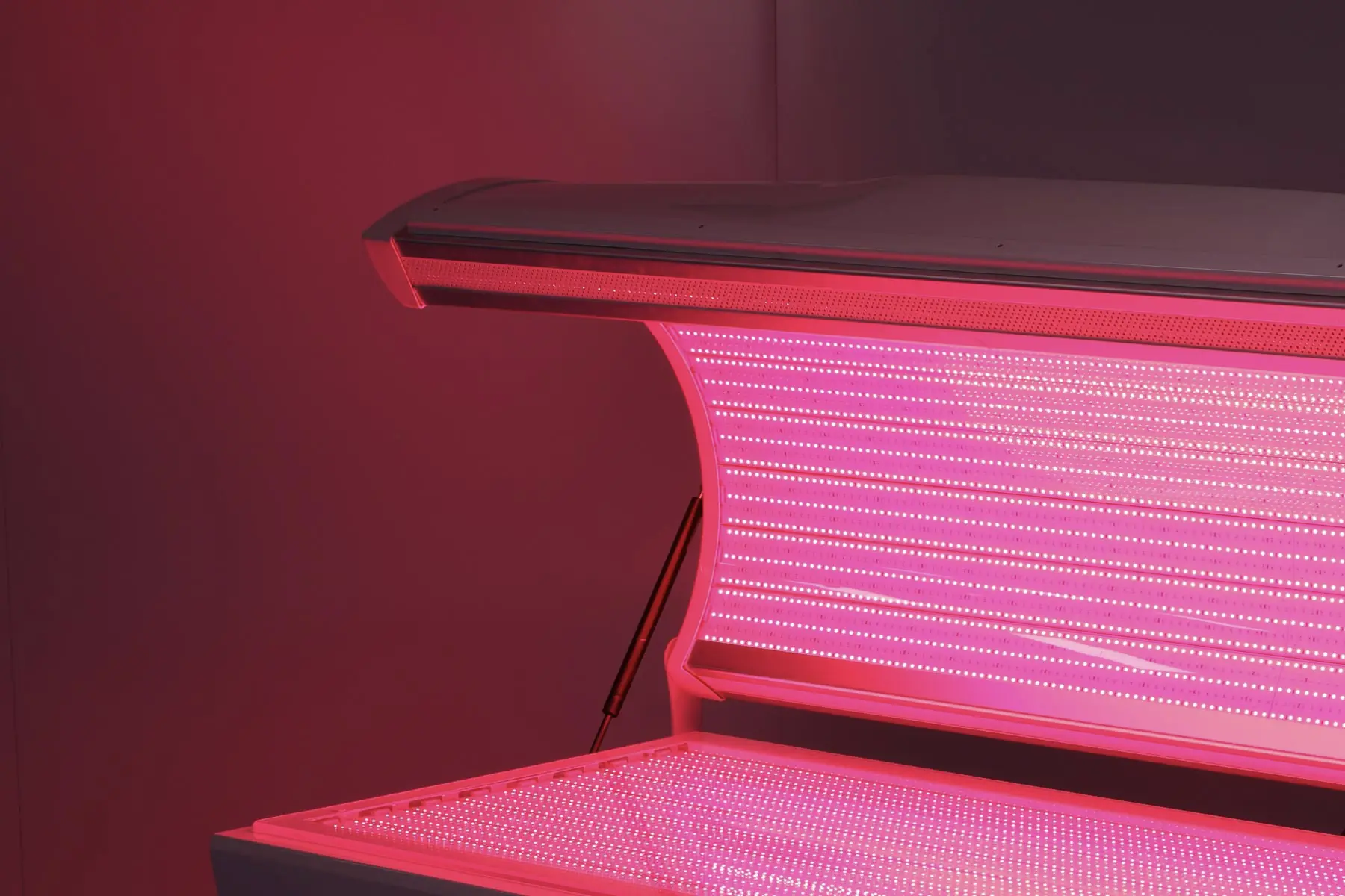 Red light terapijski krevet koji emituje crveni sjaj, ističući svoj elegantan, zakrivljen dizajn u smirenom, modernom ambijentu.