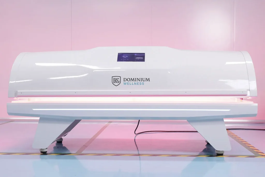 Prednji pogled na zatvorenu belu elegantnu visokotehnološku hiperbaričnu kiseoničku komoru Dominium Wellness, model DWRB Comfort, koji prikazuje moderan spoljašnji dizajn.