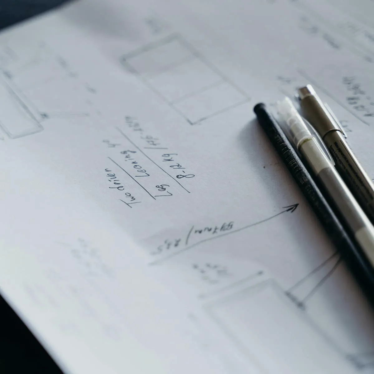 Detalj skica sa ručno crtanim tehničkim crtežima i merama, uz tri olovke koje naglašavaju proces planiranja i dizajna.